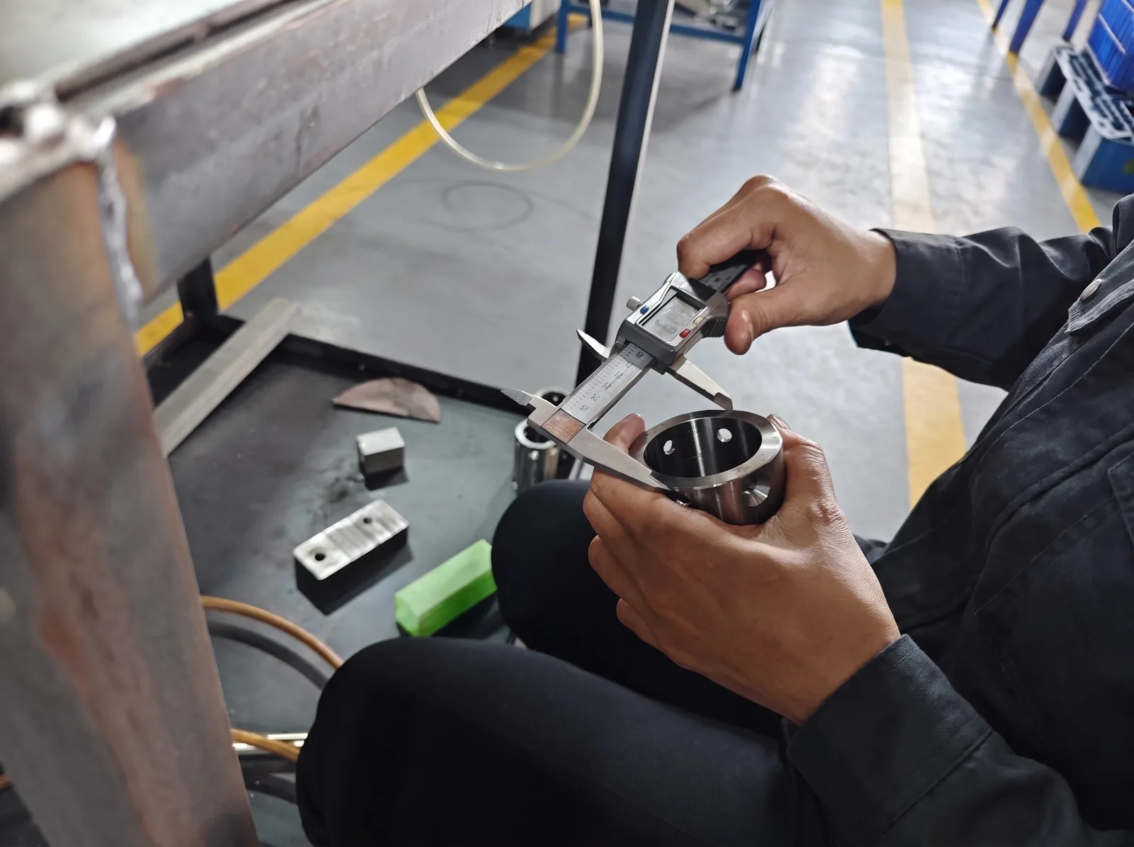 A worker measuring the bore of a machined part with a digital caliper
